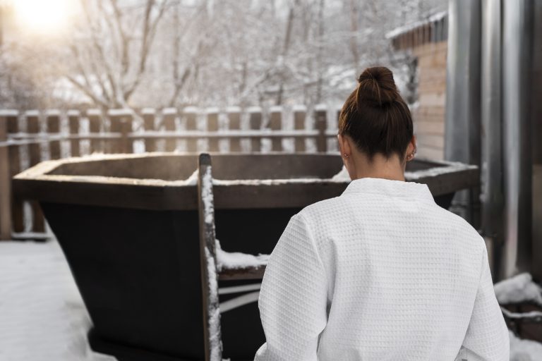 Woman in a robe entering a cold plunge tub in the snow